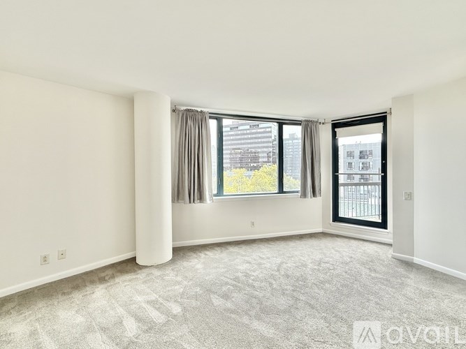 A spacious, empty room with a large window and a carpeted floor.