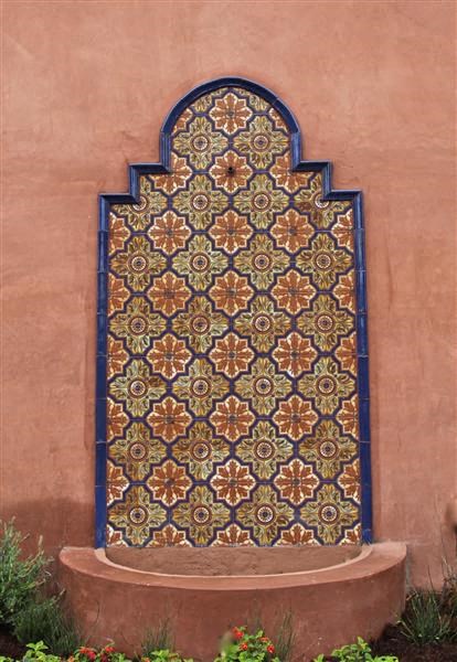 a colorful tile wall with a fountain in front of a building