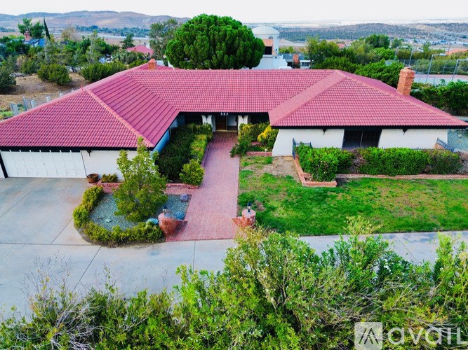 A house with a red roof and a white exterior is surrounded by greenery.