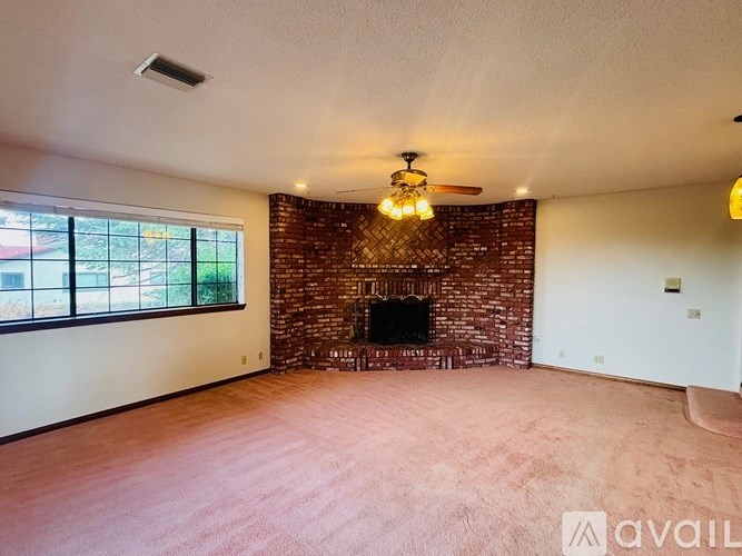 A living room with a brick fireplace and a ceiling fan.