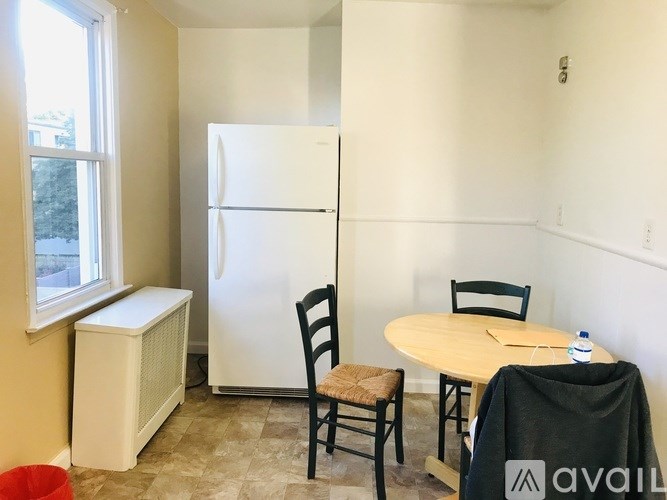A kitchen with a white fridge, a table with two chairs, and a window.