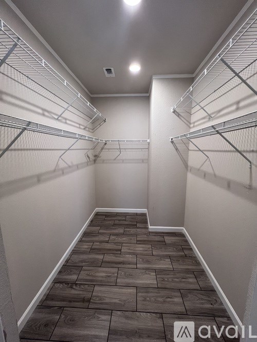 A long, narrow walk-in closet with wooden floors and white shelving.