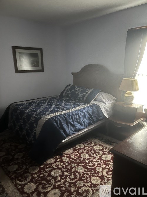 A bed with a blue comforter and a pillow is on a patterned rug in a room with a wooden headboard.