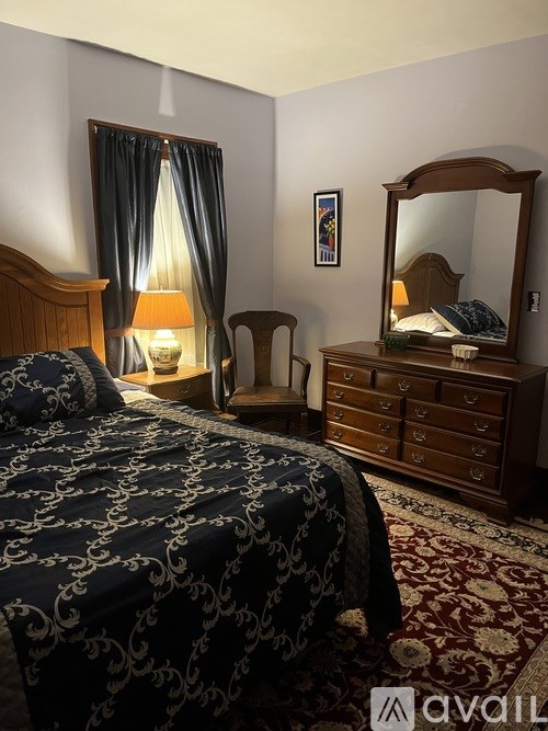 A bedroom with a bed, a chair, a dresser, and a mirror.