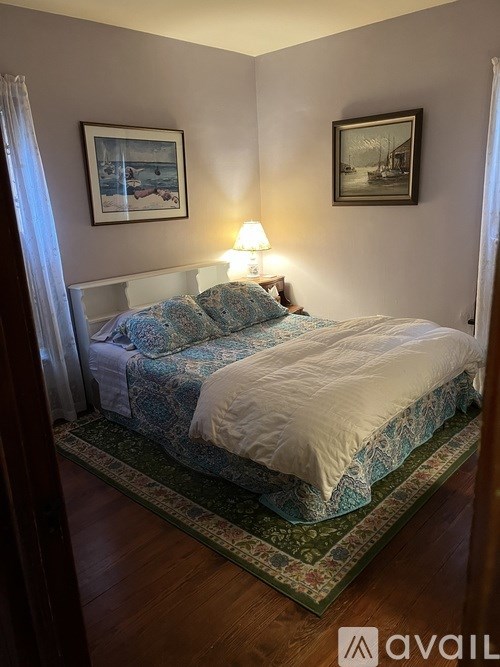 A bed with a white comforter and a blue patterned blanket is in a room with two pictures on the wall.