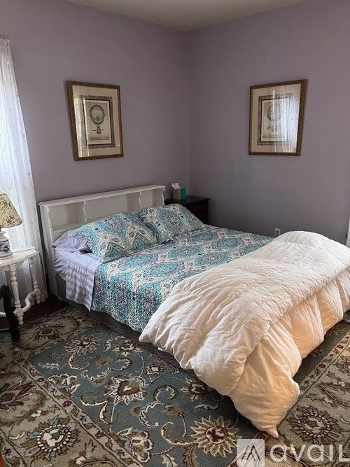 A bed with a white comforter and a blue and white patterned blanket is in the center of the image.