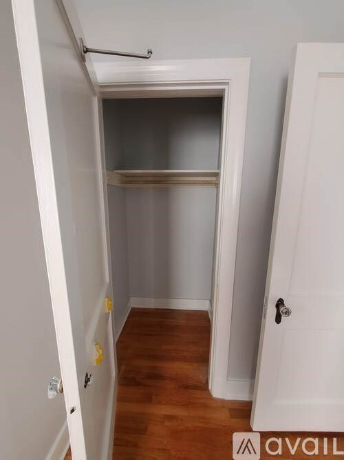 A small, empty room with a door on the right and a closet with a shelf inside.