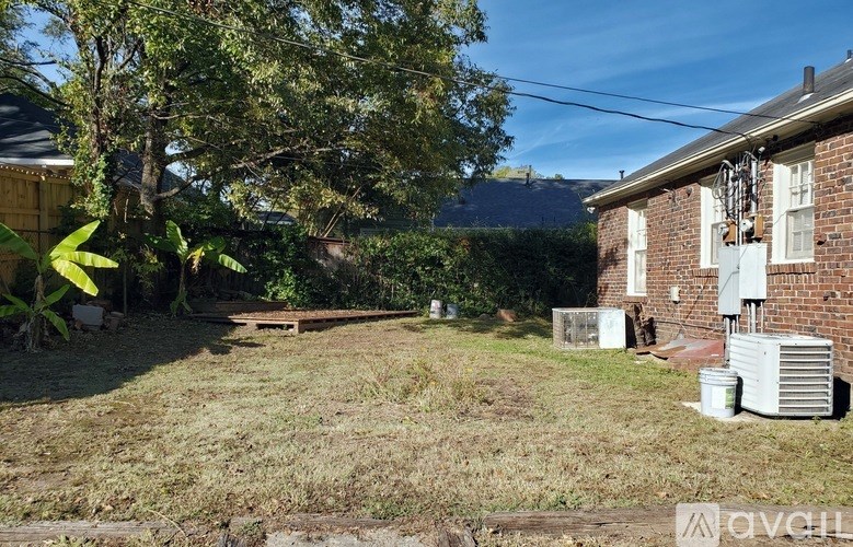 A backyard with a lawn, trees, and a house with an air conditioning unit.