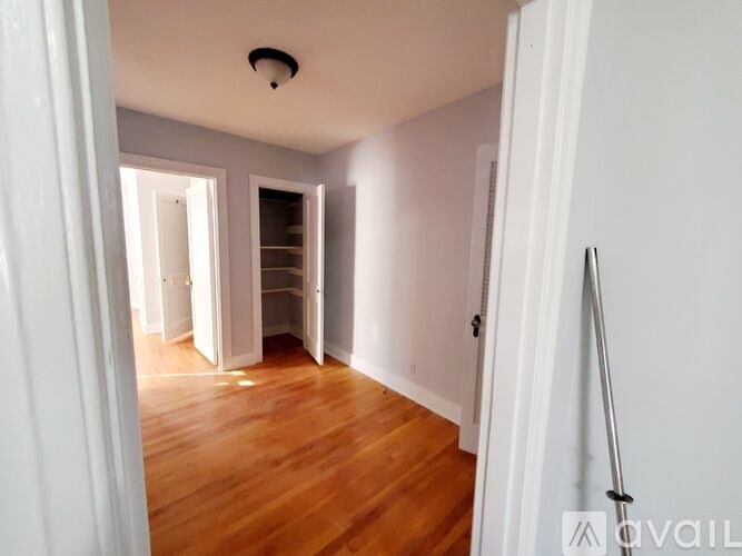 A room with wooden floors and white walls, with a doorway leading to another room.