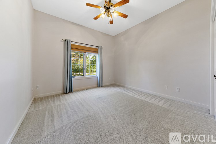 A spacious room with a ceiling fan and a window with curtains.