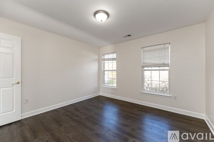 A spacious room with wooden flooring and two windows.