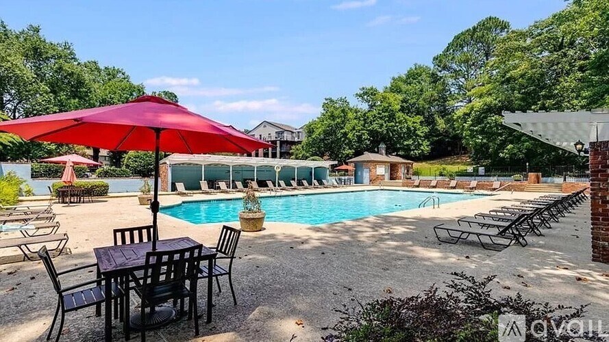 A pool area with a red umbrella and chairs.