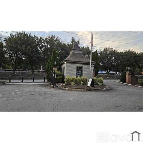 A small building with a flag on top is surrounded by a paved area and some greenery.