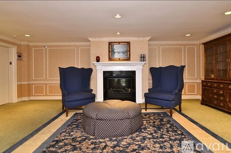 A living room with a fireplace, two chairs and a round ottoman.