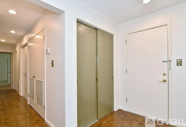 A hallway with white walls and wooden floors, leading to a white door.