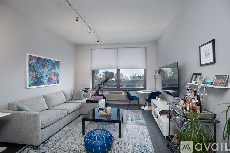 A living room with a grey couch, a blue ottoman, a coffee table, and a painting on the wall.