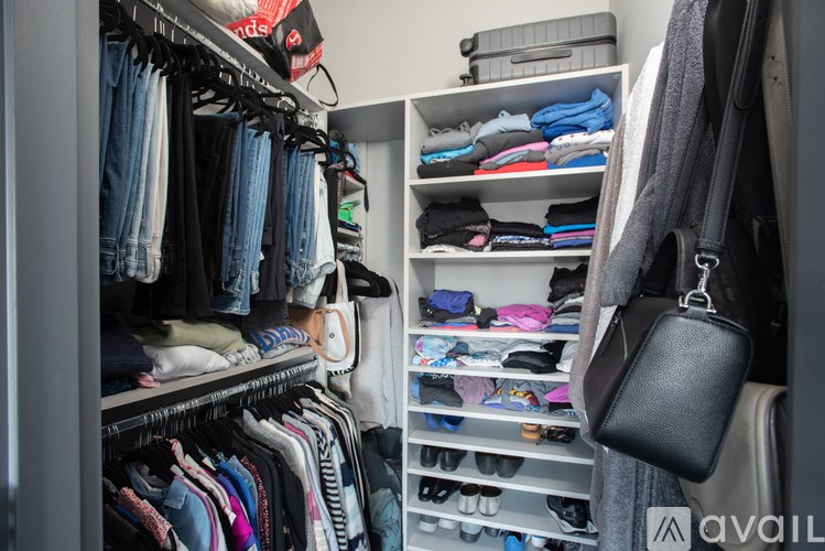 A black purse hangs on a hanger in a closet full of clothes.