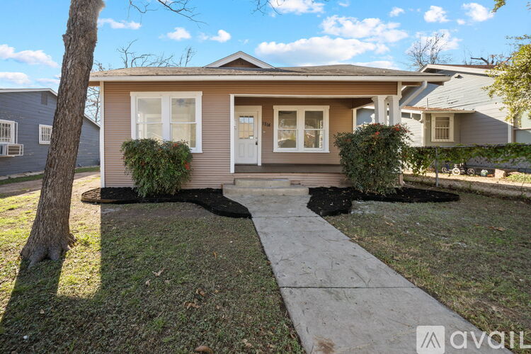 A small house with a white door and windows is surrounded by a lawn and a sidewalk.