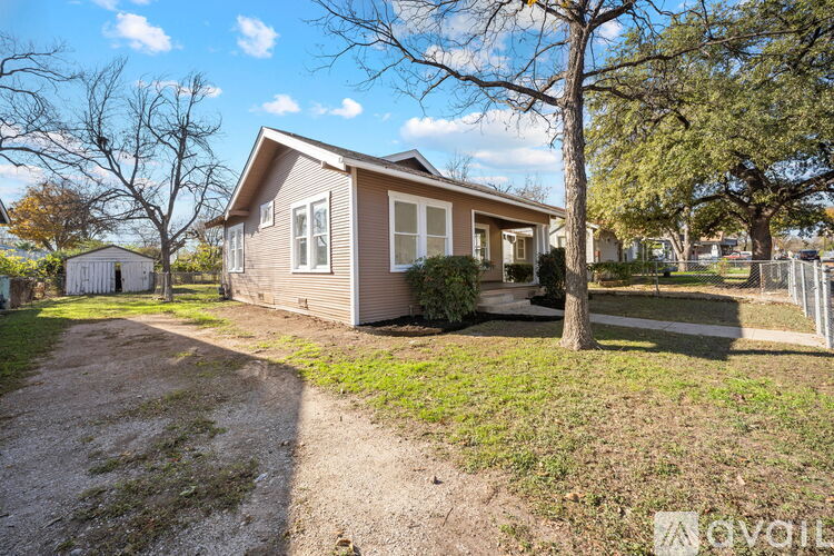 A house with a brown roof and a grey wall is surrounded by a gravel driveway and a grassy area.