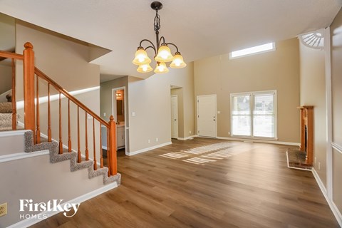 A well-lit, spacious room with wooden floors and a staircase with a wooden railing.