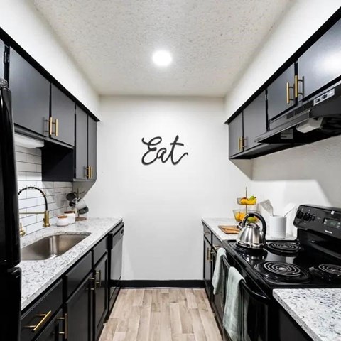 A kitchen with black cabinets and a white wall with the word Eat written on it.