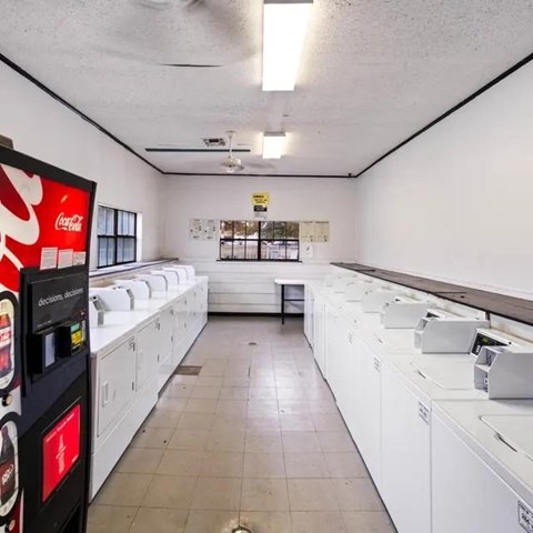 A Coca-Cola vending machine is on the left in a laundromat with rows of washing machines.