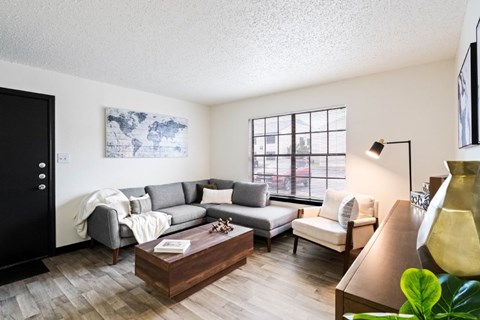 A living room with a grey couch, a coffee table, and a large window.