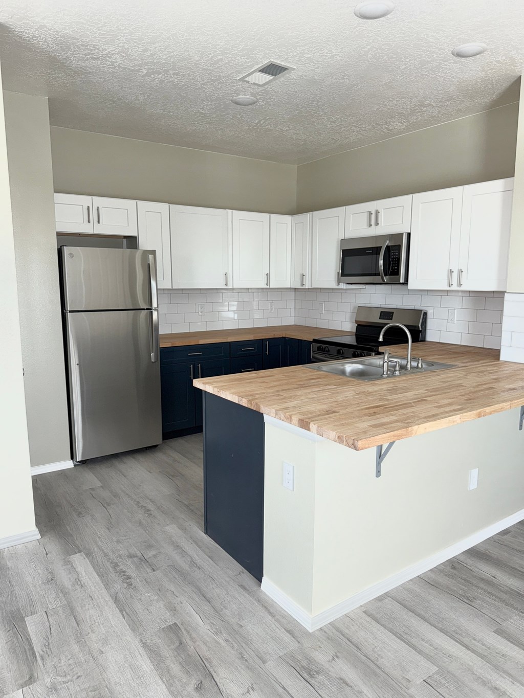 A kitchen with a wooden countertop and a stainless steel refrigerator.