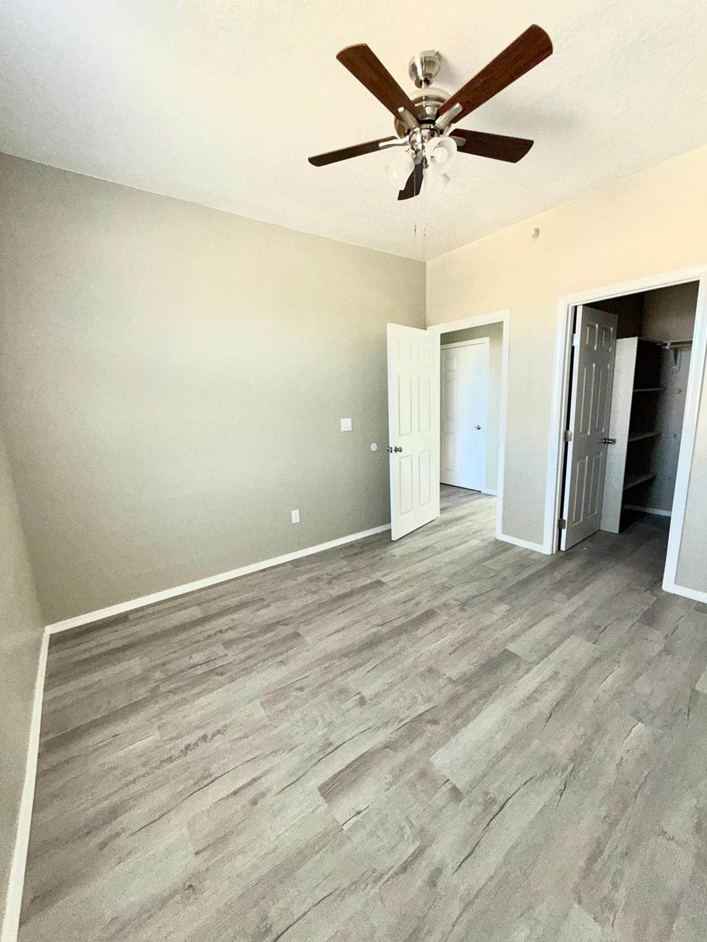 A room with a ceiling fan and light fixture, and a doorway leading to another room.