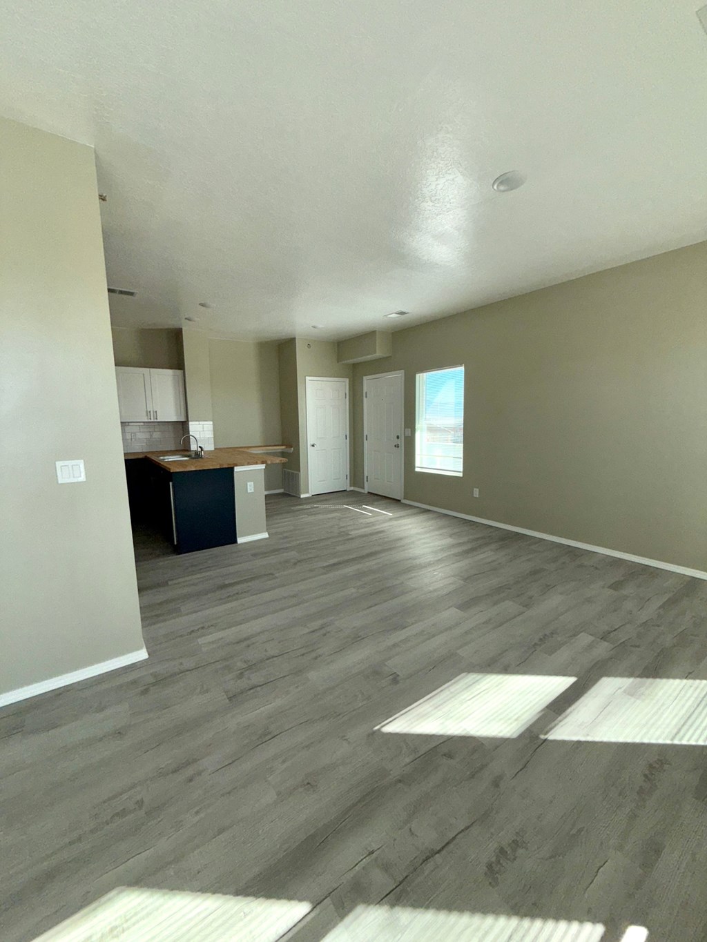 A room with wooden flooring and a kitchen area in the background.