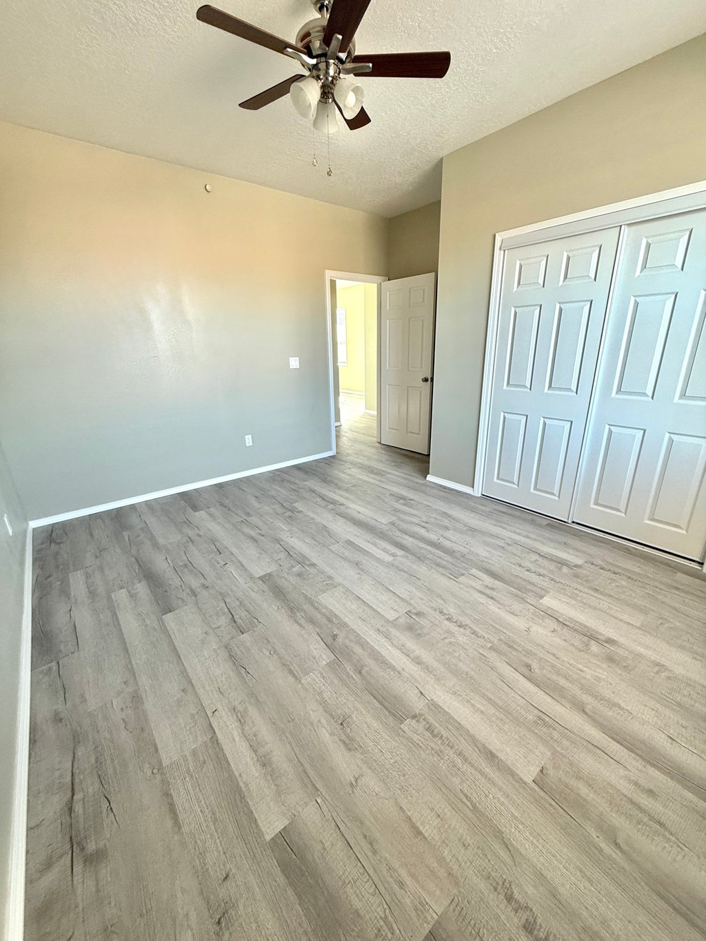 A room with a ceiling fan and light, hardwood floors, and a white door.