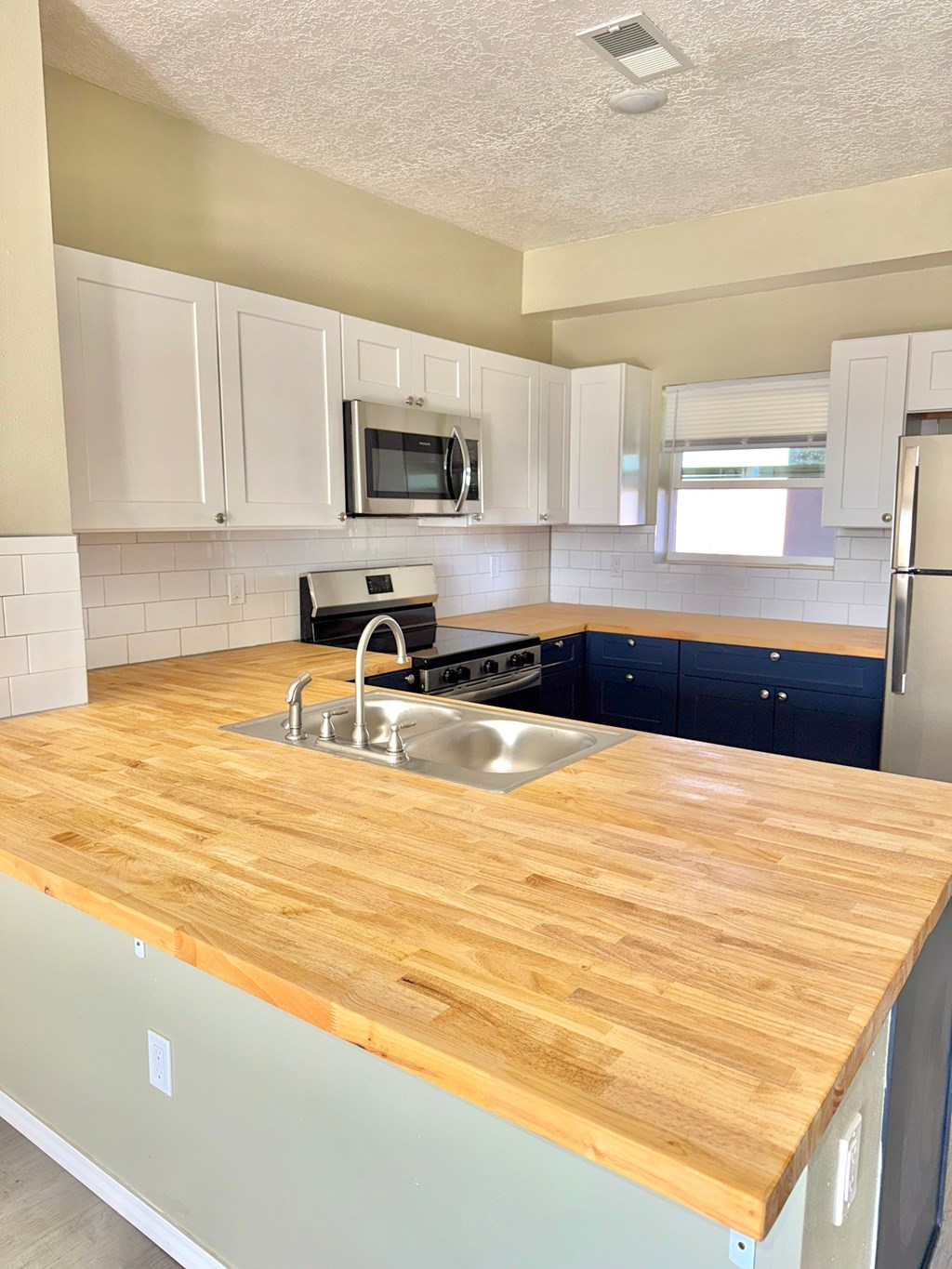 A kitchen with a wooden countertop and a stainless steel sink.