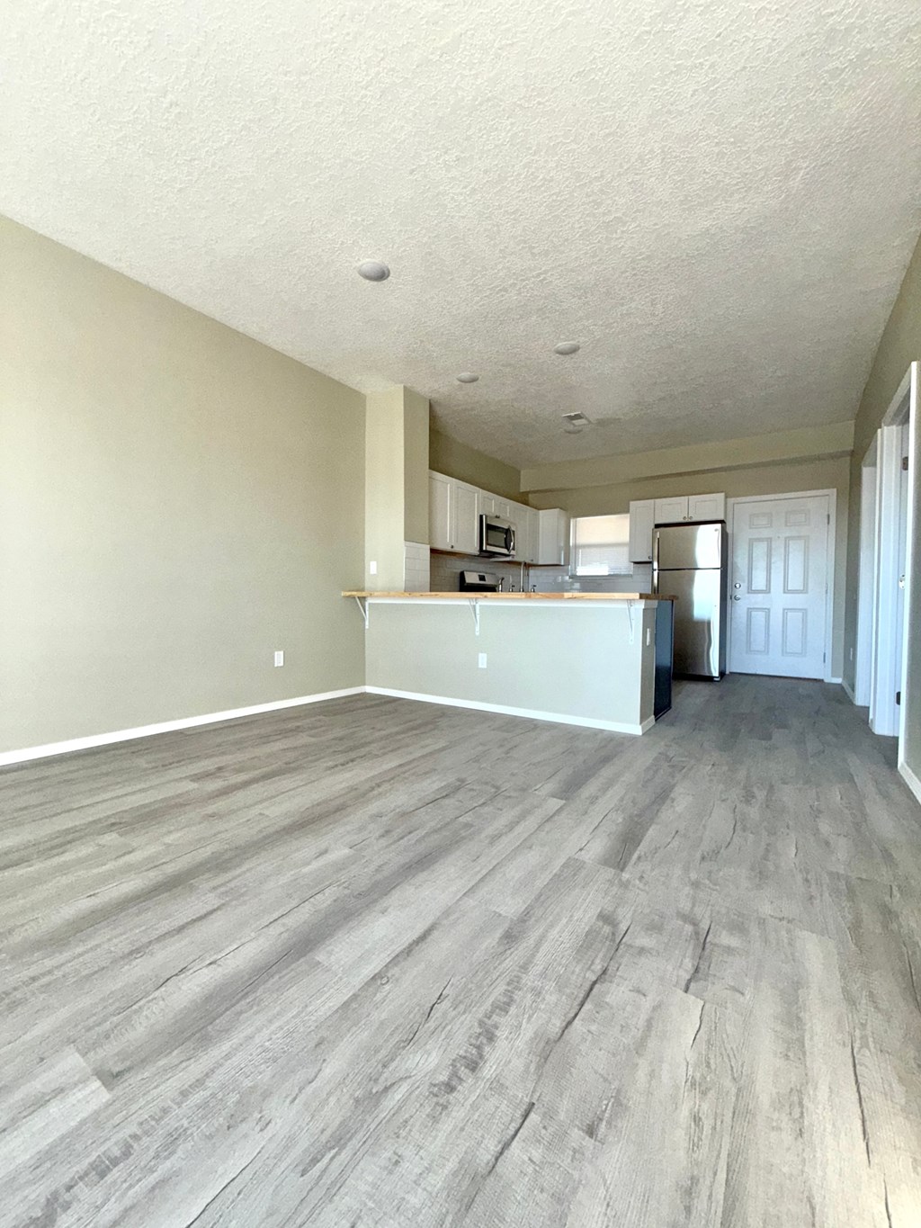 A room with wooden flooring and a kitchen area in the background.