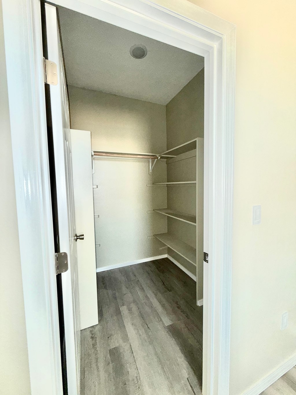 A white door is open to a room with a white wall and a white closet with shelves.
