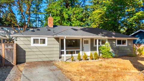 A house with a grey exterior and a white door is surrounded by trees.