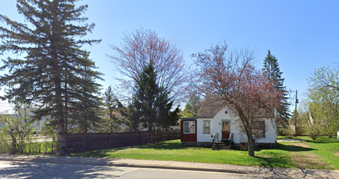 A small white house with a brown roof is surrounded by trees.