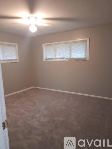 A room with a ceiling fan and two windows.