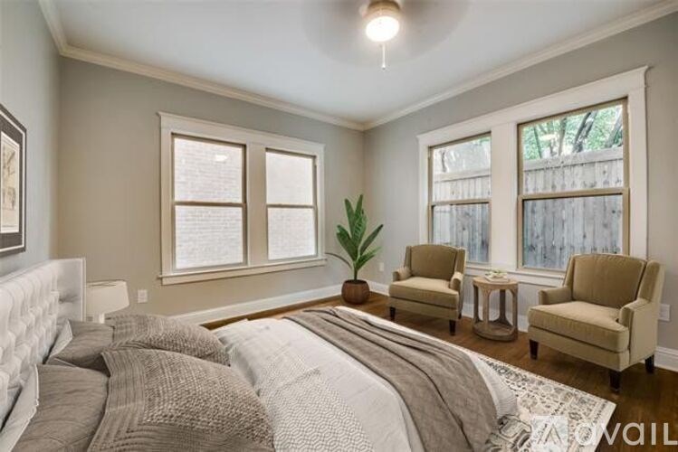 A bedroom with a bed, two chairs, and a plant.