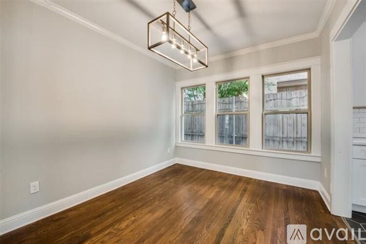 A room with wooden floors and a window with a view of a fence and trees.