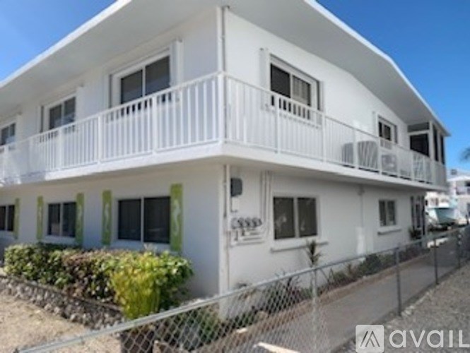 A white two-story house with a balcony and a fence.
