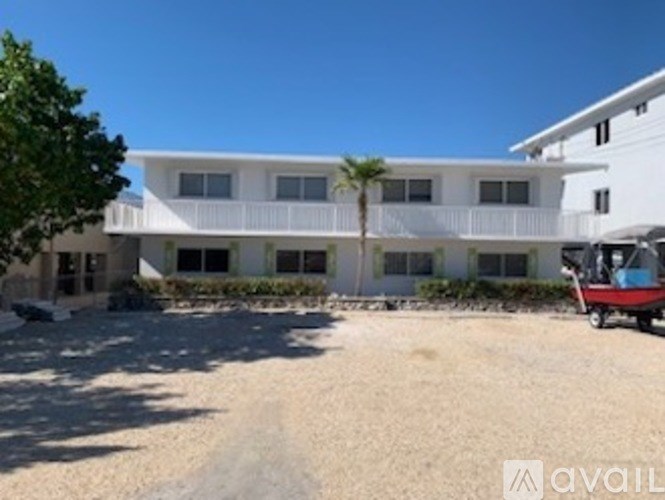 A white building with a balcony and a tree in front of it.