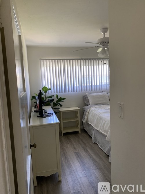 A small bedroom with a bed, nightstand, and a plant on a dresser.