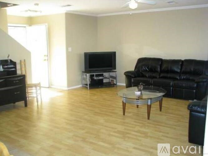 A living room with a black leather couch, a glass coffee table, and a flat screen TV.