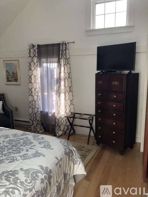 A bedroom with a bed, a dresser, and a window with curtains.