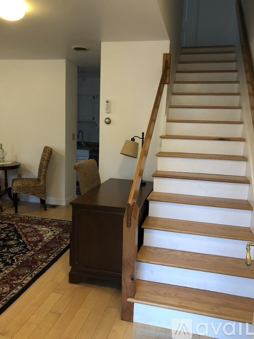A wooden staircase with a brown wooden cabinet and a rug in front of it.