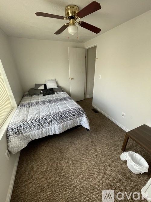A bedroom with a bed, a ceiling fan, and a small table.