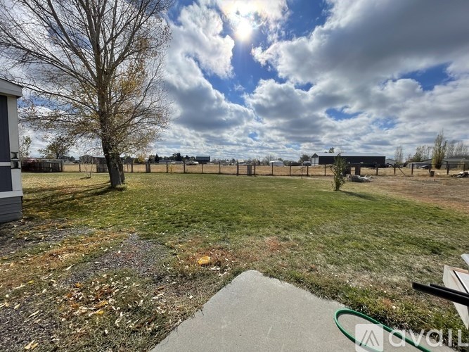 A grassy field with a building and a tree in the background.