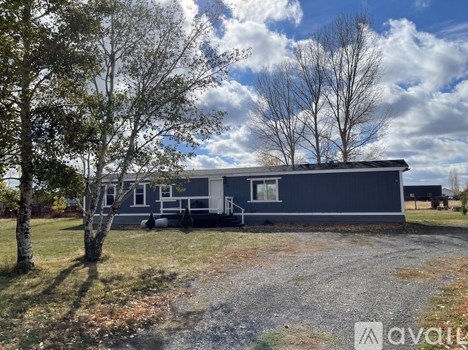 A blue mobile home sits in a grassy field with trees in the background.