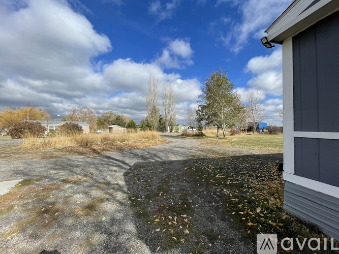 A gravel area with a building on the right and trees in the background.