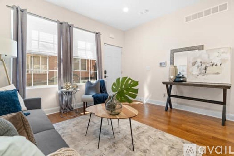 A living room with a grey couch, a wooden coffee table, and a large window with curtains.